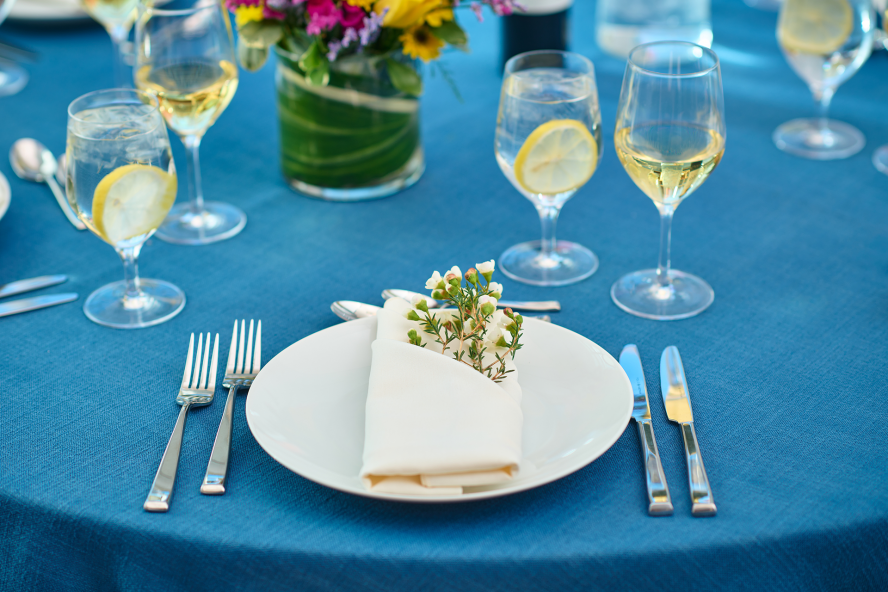 Napkin folder on a plate surrounded by filled wine glasses